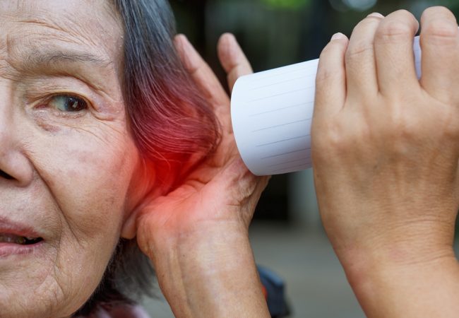 Daughter talking to hearing impaired elderly woman , using paper tube